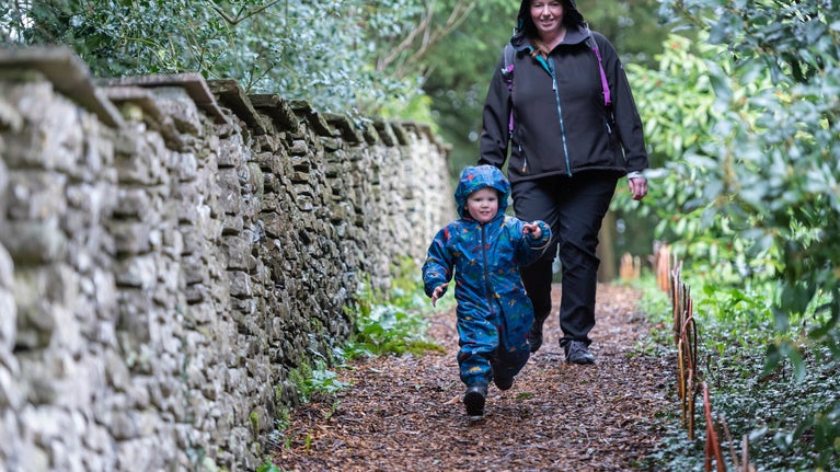 A mother and young child walking down a path at Sizergh during the winter. The child is wearing a blue snowsuit, and the mother is wearing a waterproof coat.